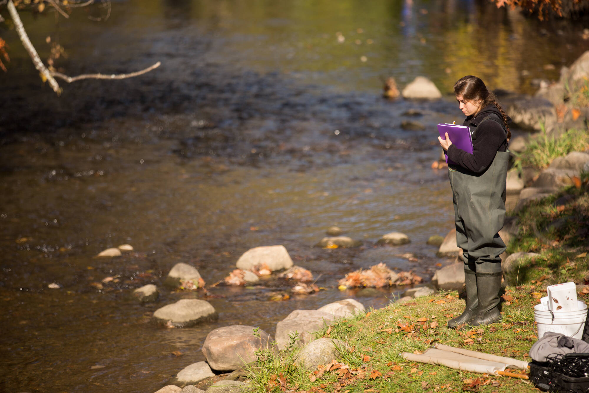 student standing in waders on the bank of a stream with rocks in it